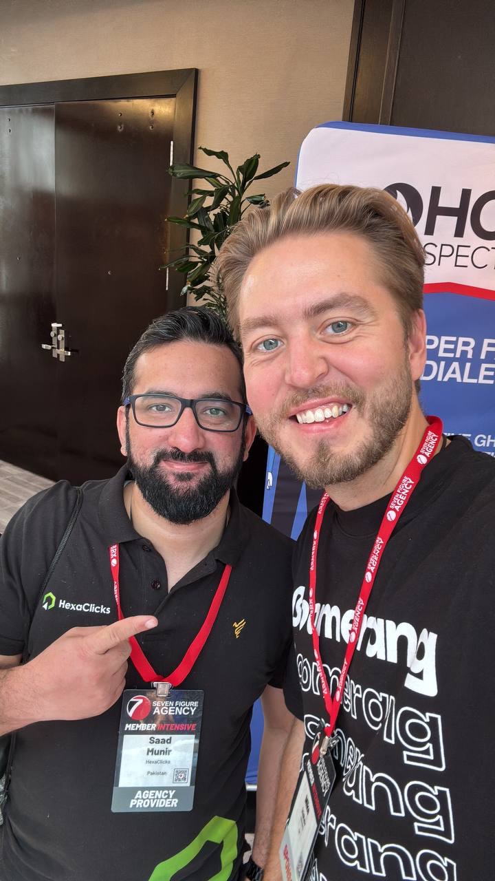 Two men smiling at the Seven Figure Agency Intensive, one in a Boomerang t-shirt, one in a HexaClicks polo