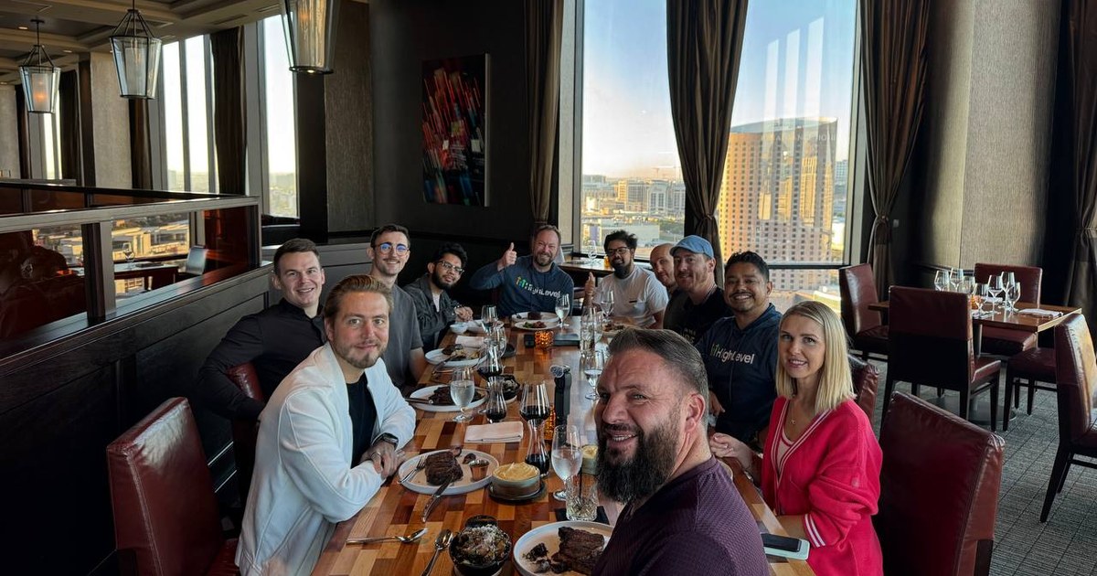 A long table of about a dozen people at a steakhouse high above a city at sunset