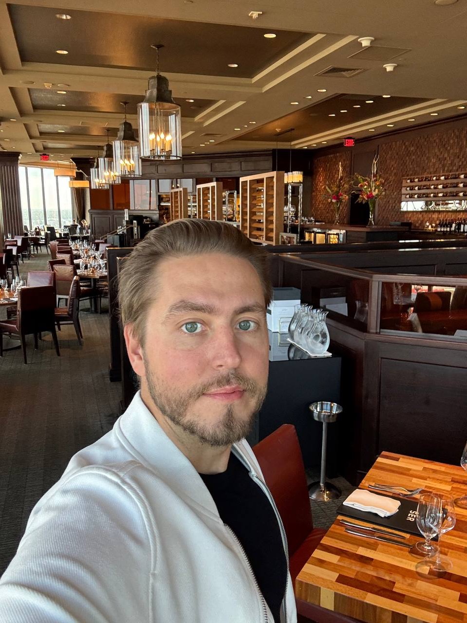 A man alone at a set table in an empty steakhouse dining room before guests arrive