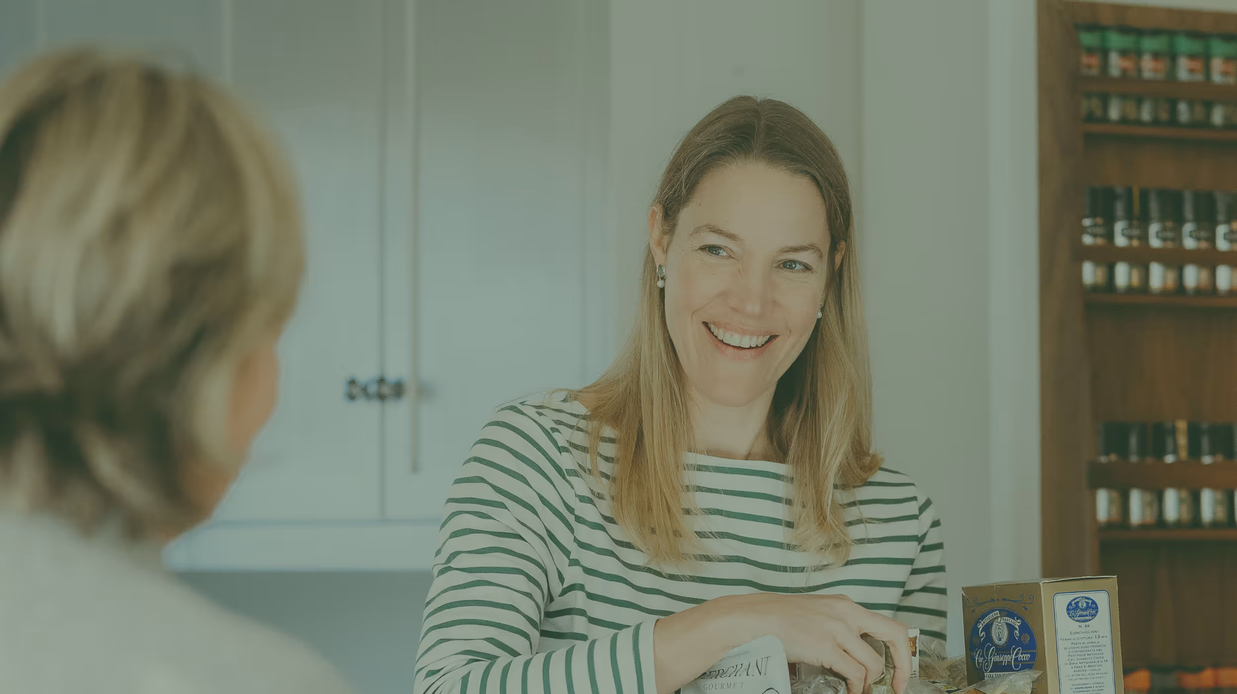 Smiling woman in striped shirt handing a packaged item to another person indoors.