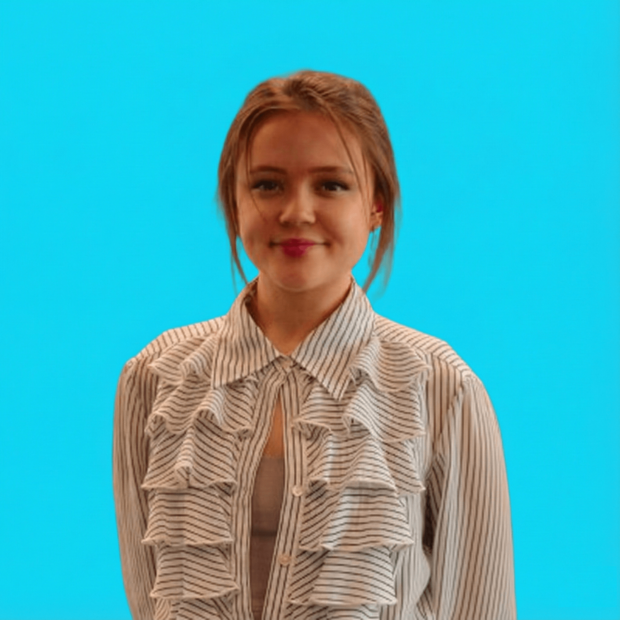 Young woman with light brown hair wearing a striped blouse with ruffles, against a bright blue background.
