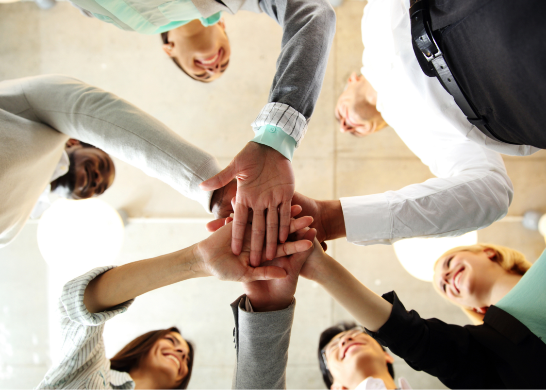 Six diverse businesspeople smiling in a circle with hands stacked in the center.