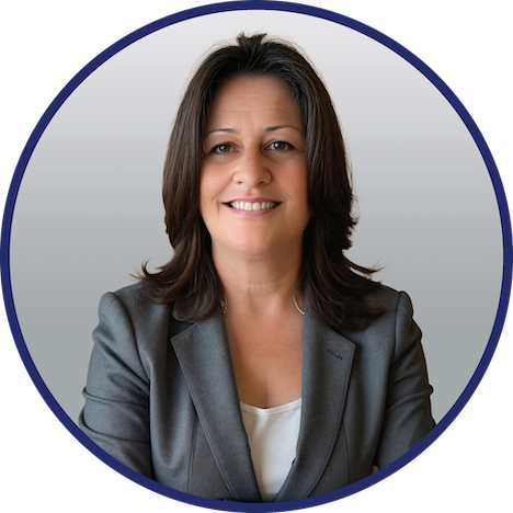 Professional headshot of Janet Hazelwood, wearing a white blouse and grey blazer, posed against a gray gradient background with a navy circular border.