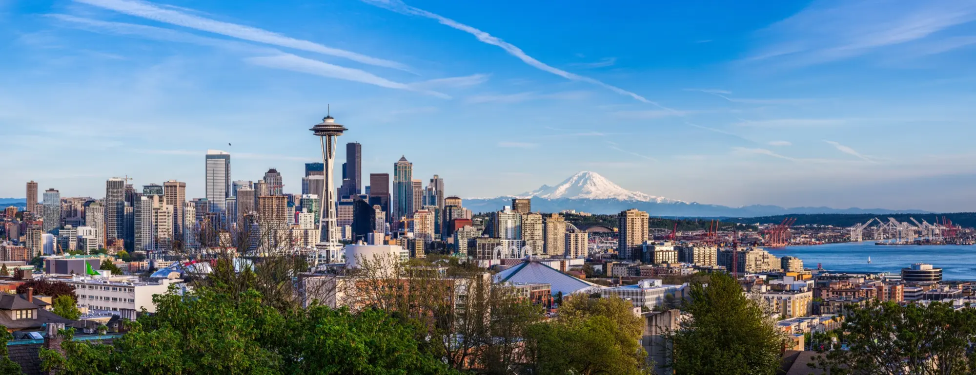 Seattle skyline featuring the Space Needle with Mount Rainier in the background under a clear blue sky.