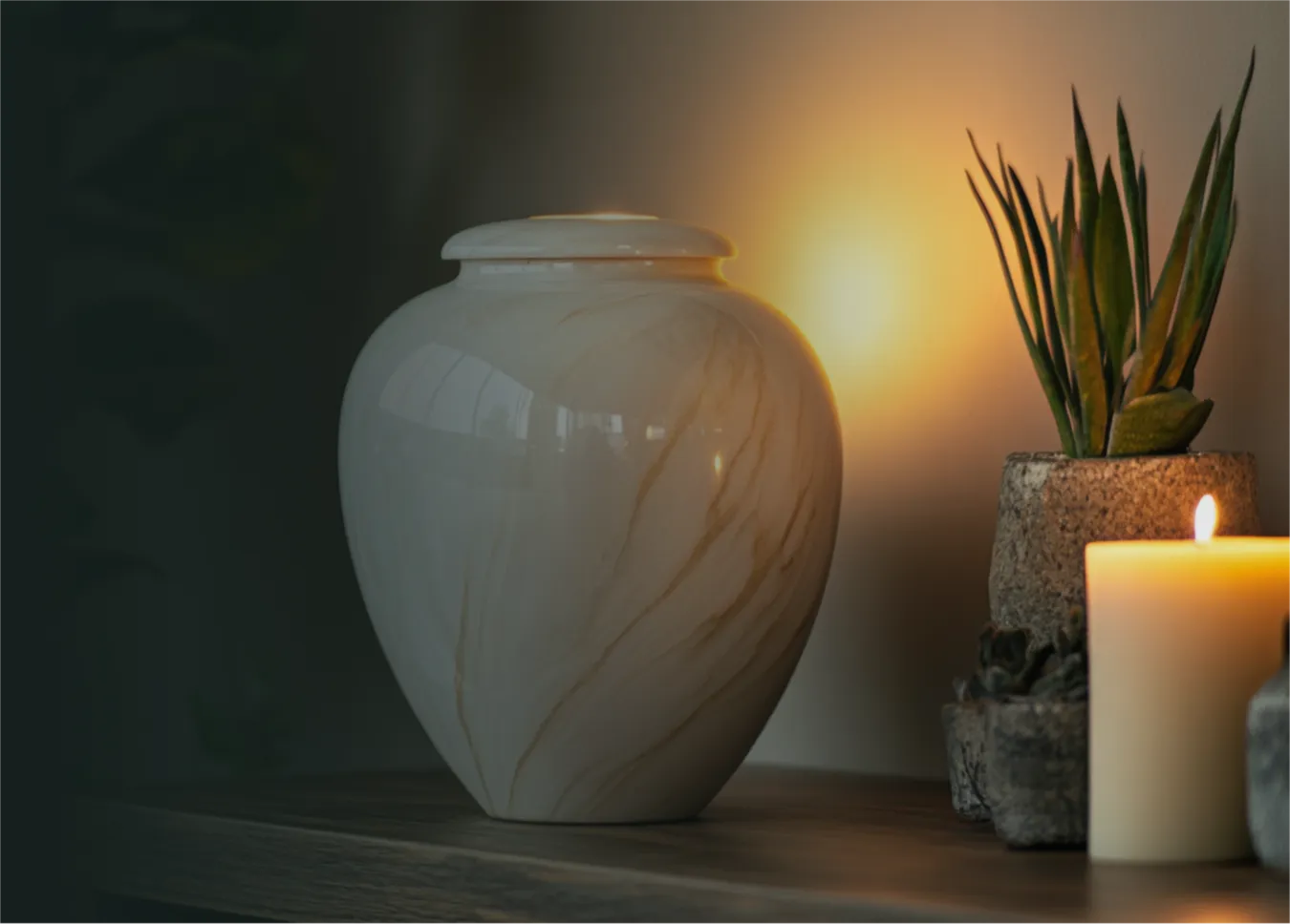 Marble urn on a wooden shelf beside a lit candle and a potted succulent plant.