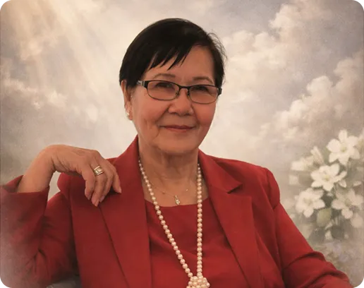 Elderly woman with glasses wearing a red blazer and pearl necklace, seated with a floral background.