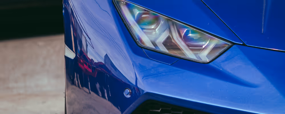 Gros plan sur l'avant d'une voiture de sport bleue avec un phare moderne et des reflets brillants.