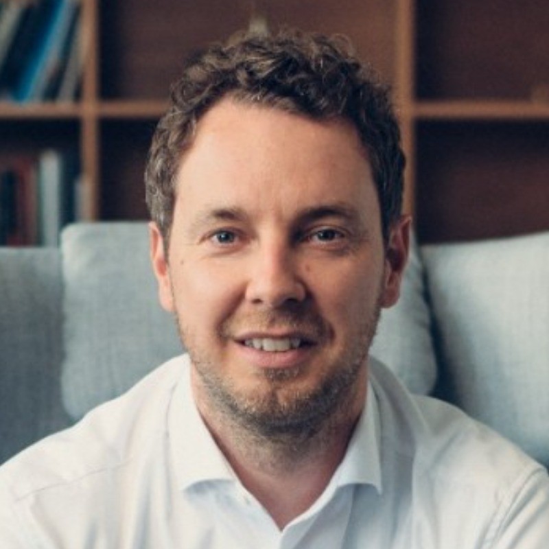 Portrait of Christoph Hesse of Greenblocks, seated on a couch with a bookshelf in the background. greenblocks testimonial on gridX HEMS enabling prosumer energy independence through automated energy management and regulatory compliance
