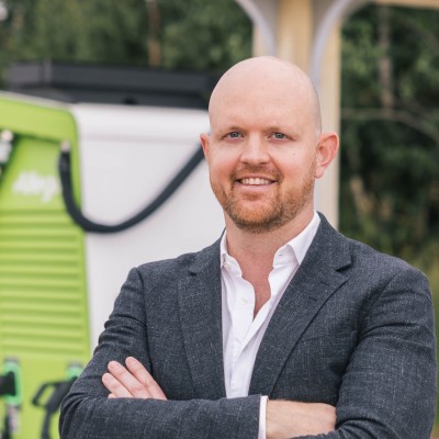 Portrait of Guillaume Goijen, arms crossed, standing outdoors in front of a green EV charging unit.