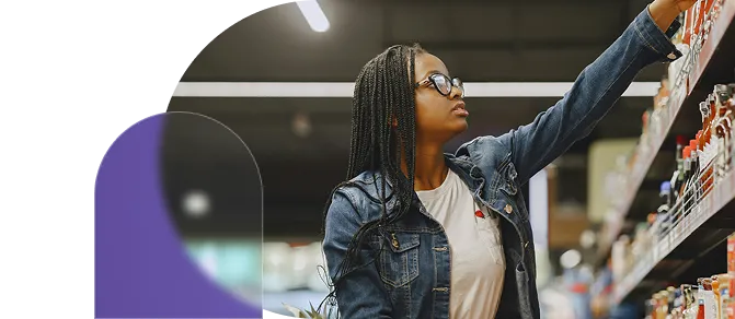 Woman with glasses and braided hair reaching for items on a grocery store shelf.