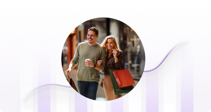 Smiling couple walking arm in arm, holding shopping bags and coffee in a city street.