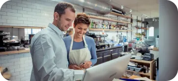 Two colleagues smiling and working together on a laptop in a modern cafe kitchen.