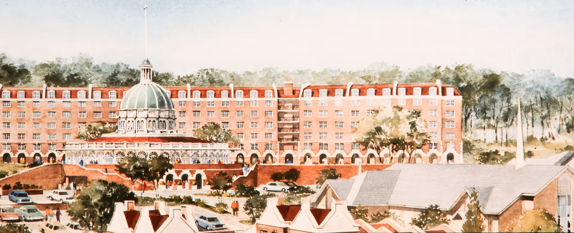 A large red-brick building with a green dome surrounded by trees and parked cars.