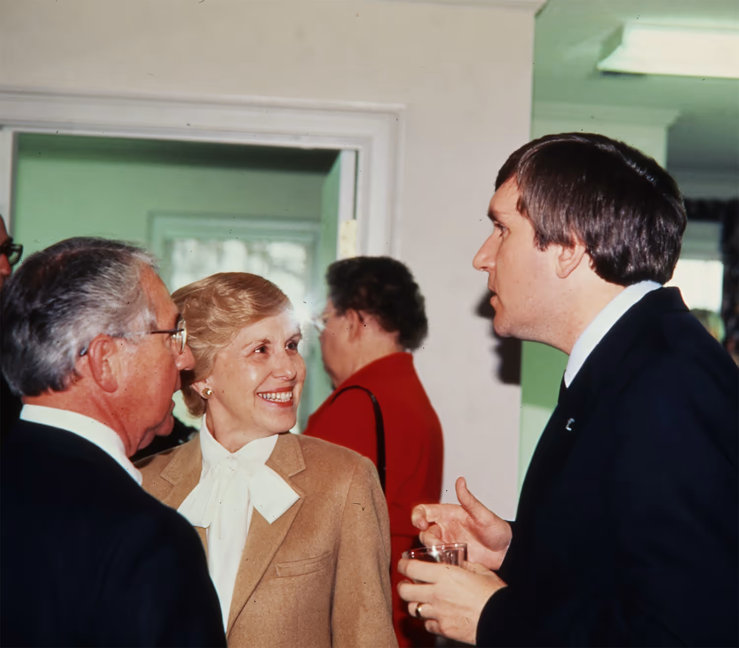 Three people engaged in a conversation at an indoor event, one holding a glass.