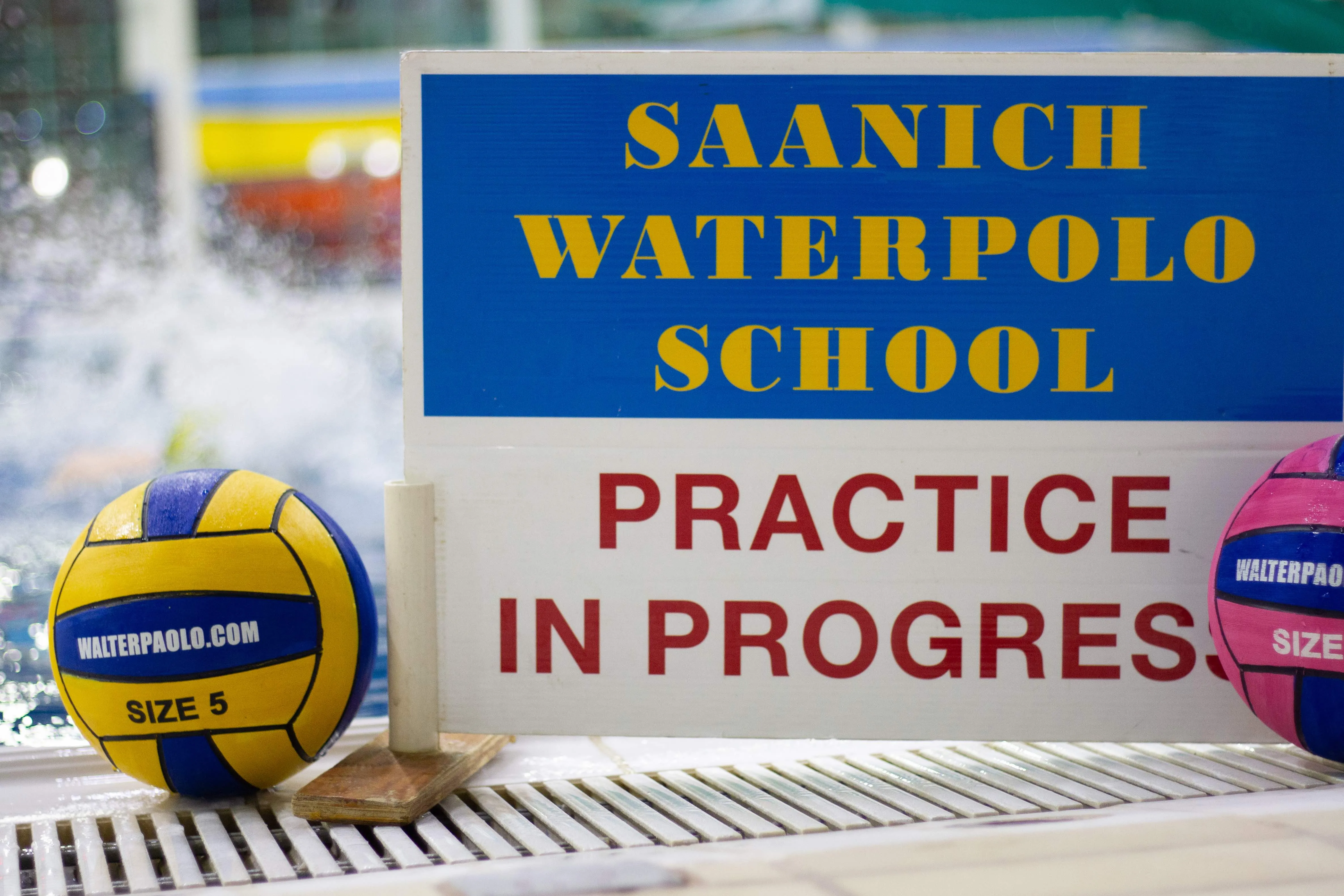 Sign reading Saanich Waterpolo School, Practice in Progress, with two balls by the pool