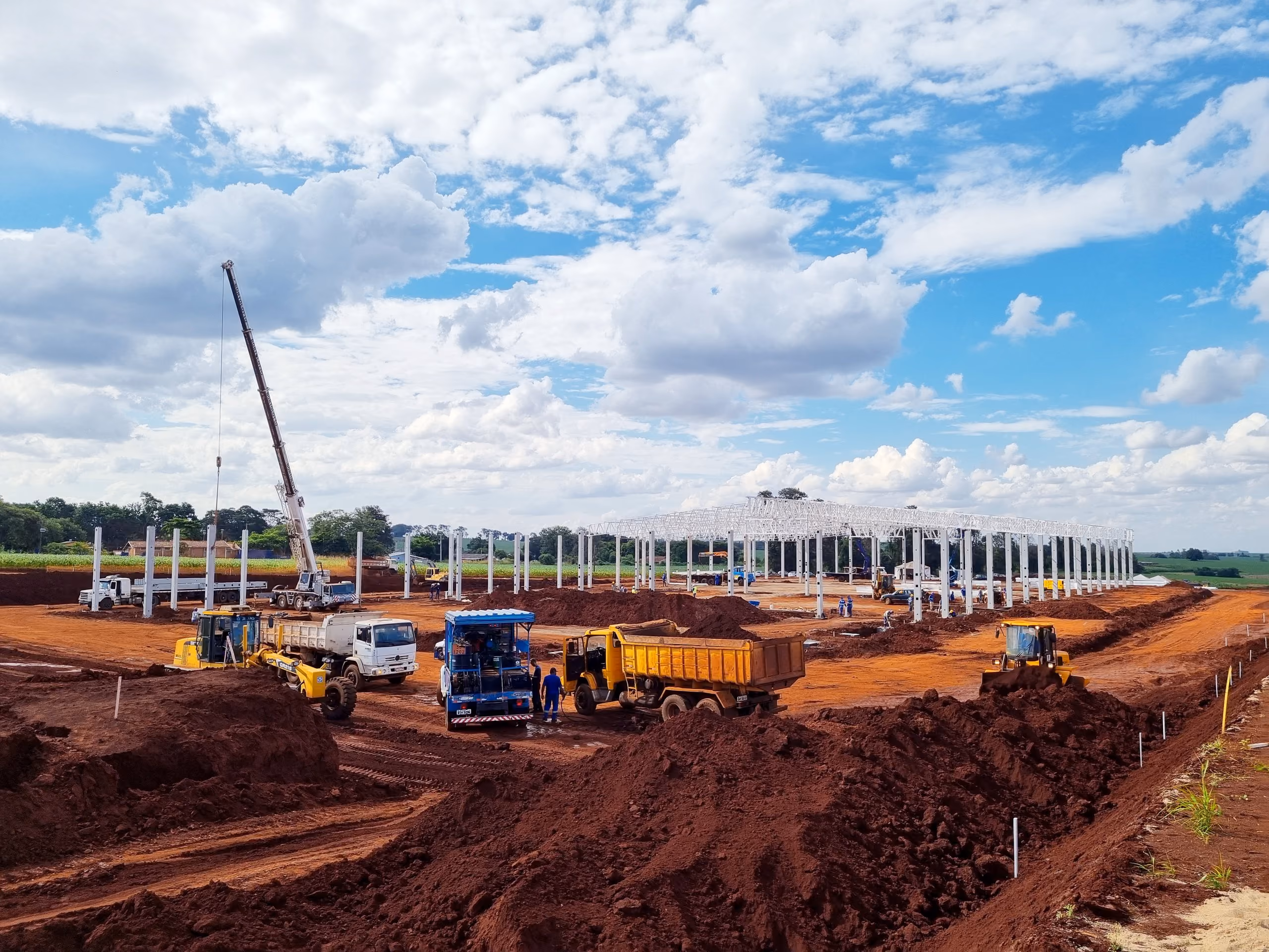 Motoniveladora, caminhões e pá carregadeira em frente de terraplanagem com guindaste ao fundo - MSE Engenharia