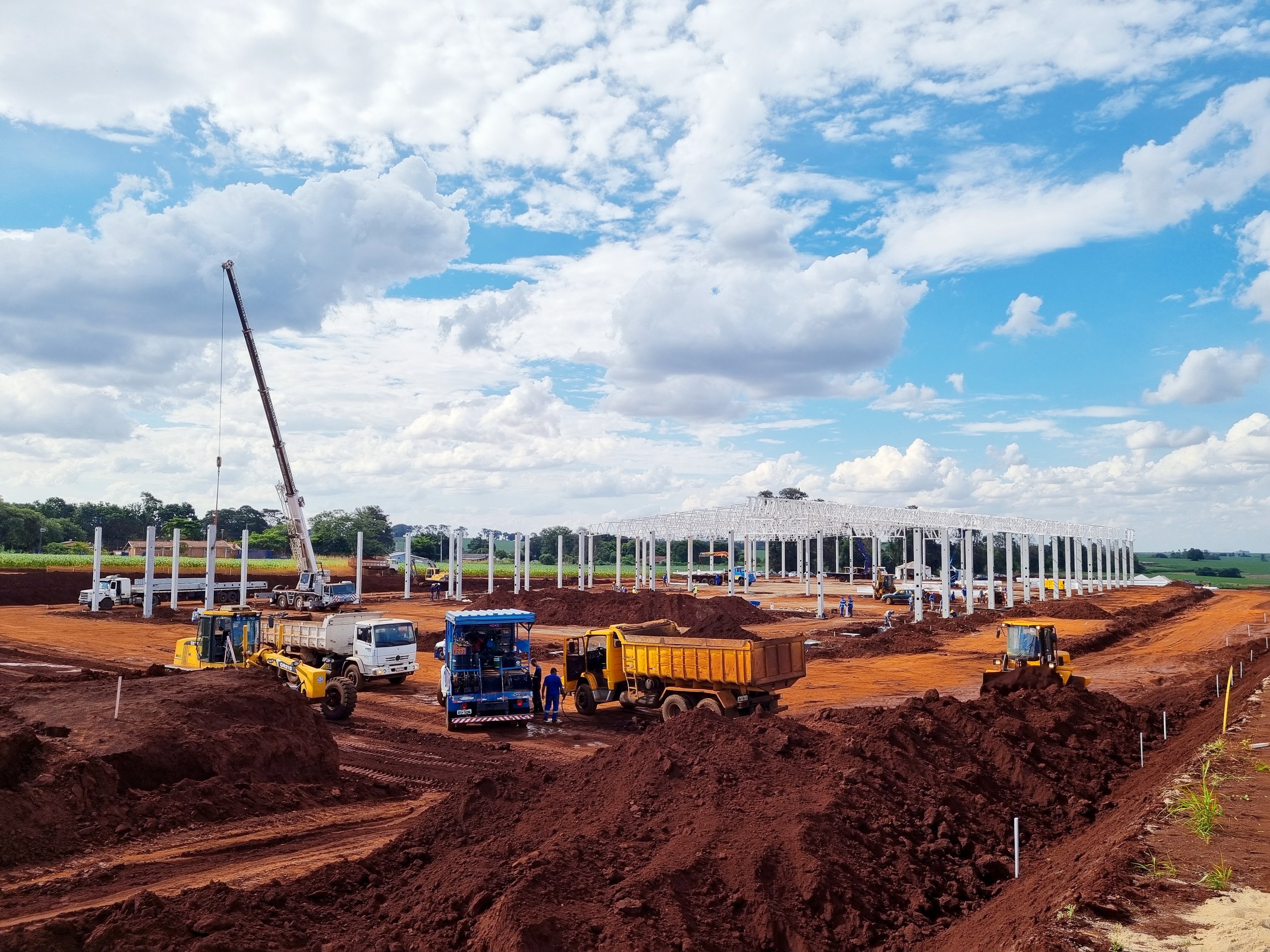 Motoniveladora, caminhões e pá carregadeira em frente de terraplanagem com guindaste ao fundo - MSE Engenharia