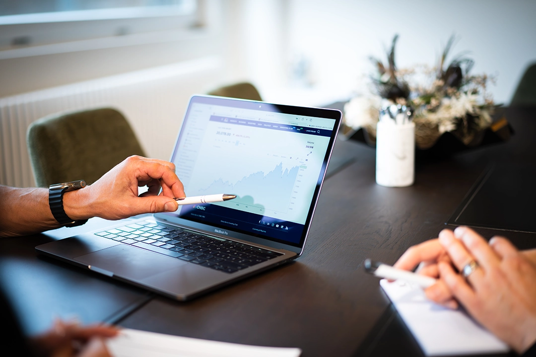 Laptop im Vordergrund worauf ein Mann zeigt.