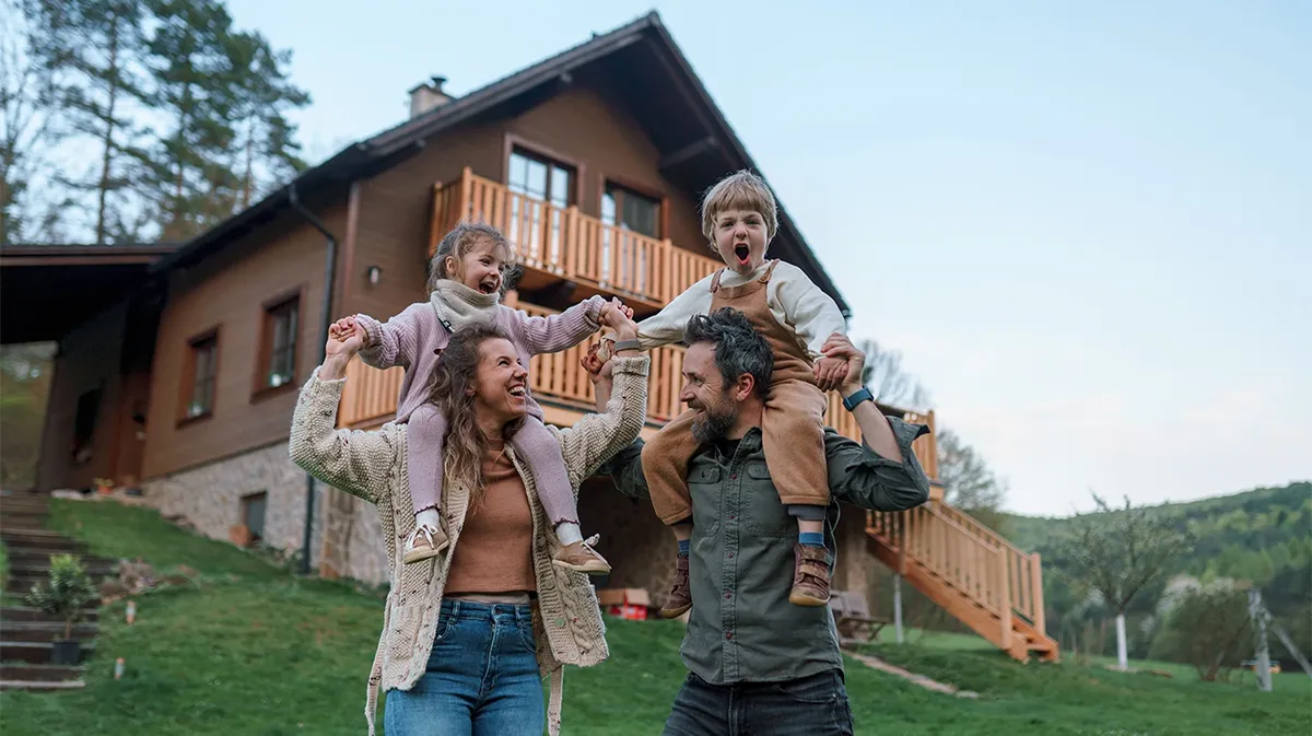 Glückliche Familie mit zwei Kindern vor einem Holzhaus