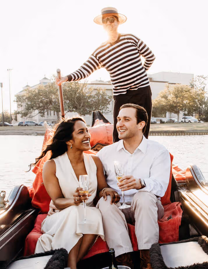 A man and woman are sitting in a boat, holding wine glasses.