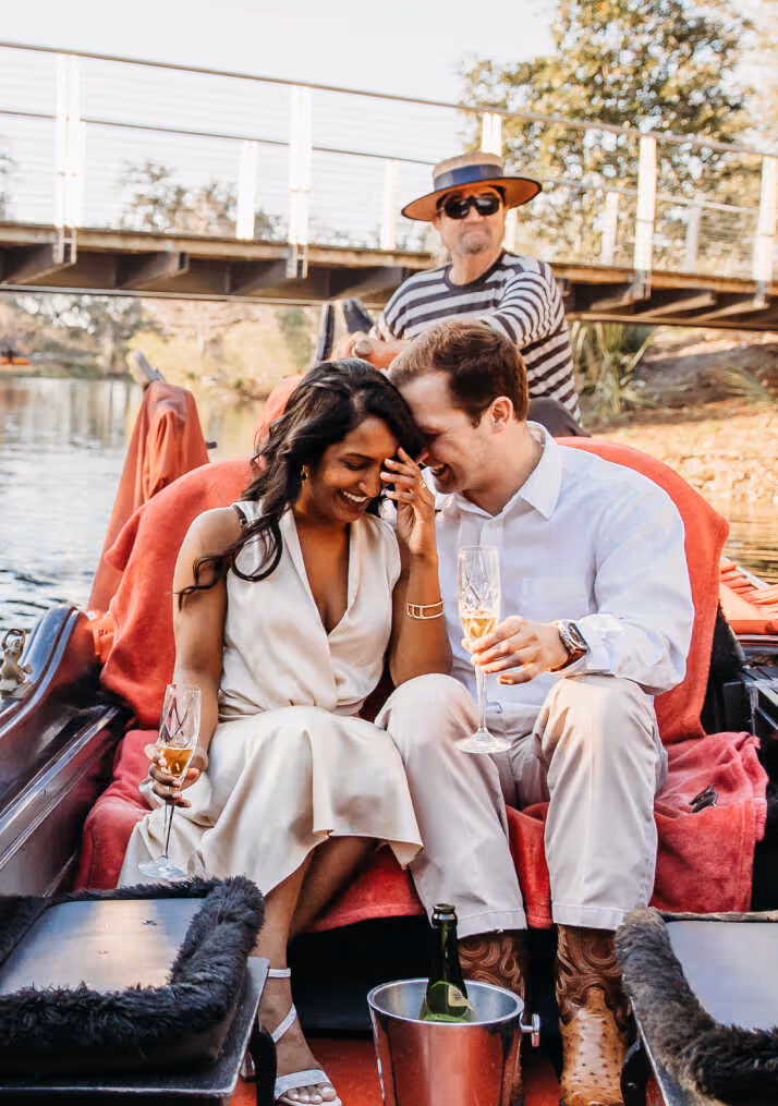 A man and woman are sitting on a boat, drinking champagne.