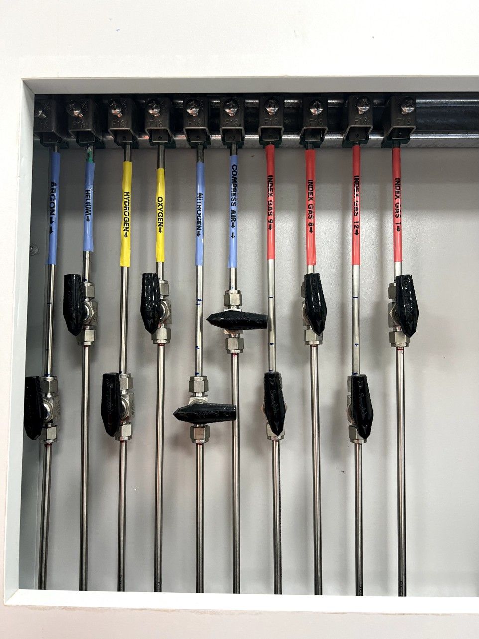 A rack of laboratory equipment featuring multiple long, slender rods with black handles and various colored caps (blue, yellow, red), likely used for sample handling or testing.

