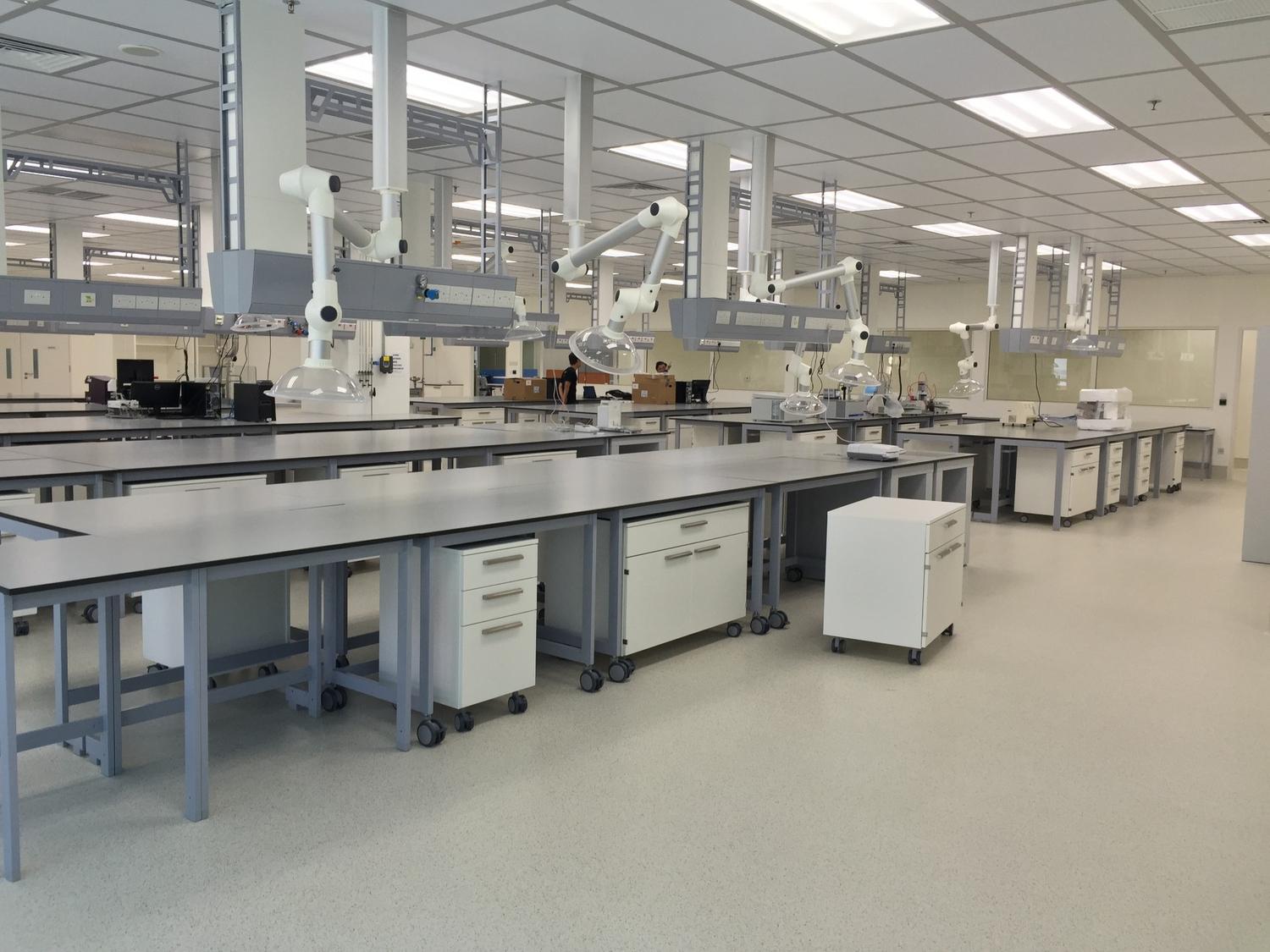 A wide view of a modern, clean laboratory with multiple lab benches, white cabinets on wheels, and overhead exhaust hoods.