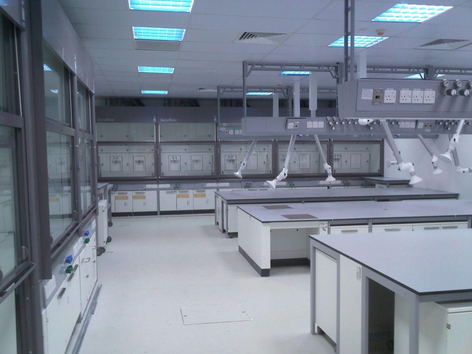 Interior of a modern, clean laboratory with multiple fume hoods, workbenches, and overhead lighting.