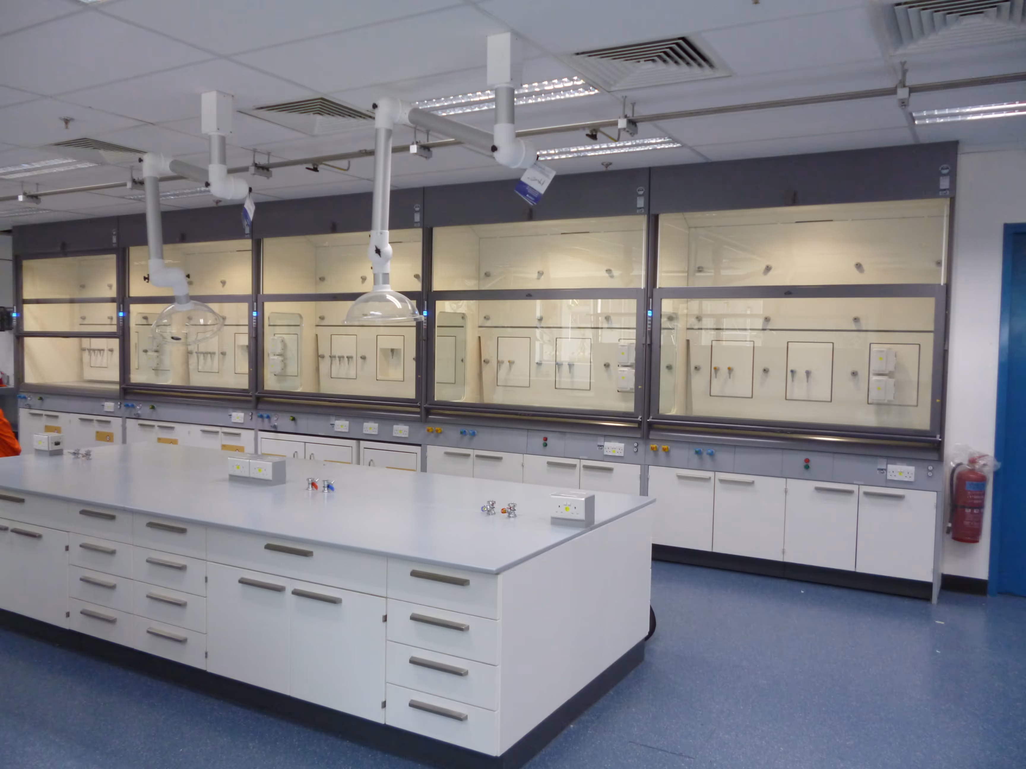 Clean, modern scientific laboratory with white fume hoods and workbenches