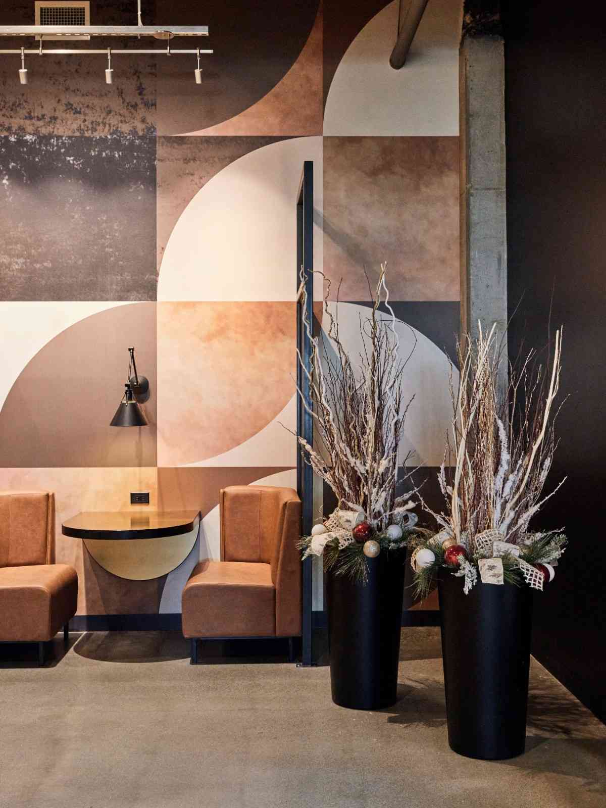 Holiday planters with frosted branches and ornaments in a modern lobby.