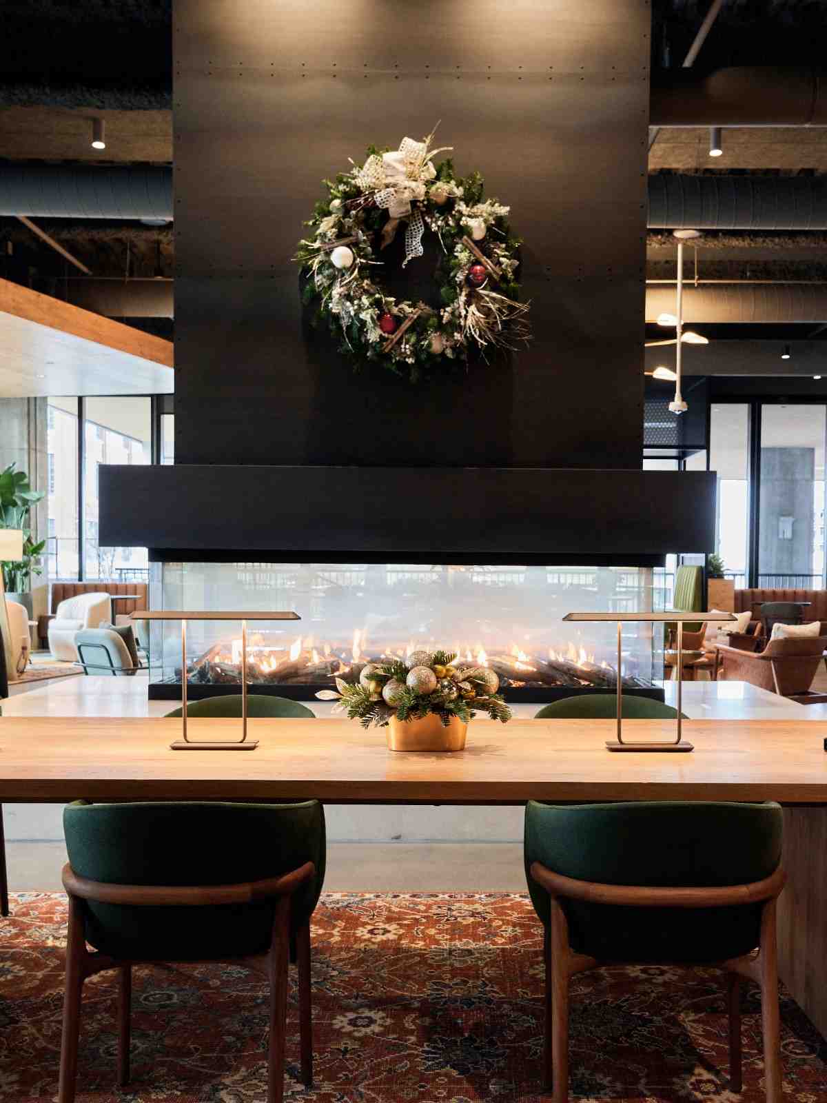 Holiday wreath and festive centerpiece displayed by a modern fireplace in a lobby.