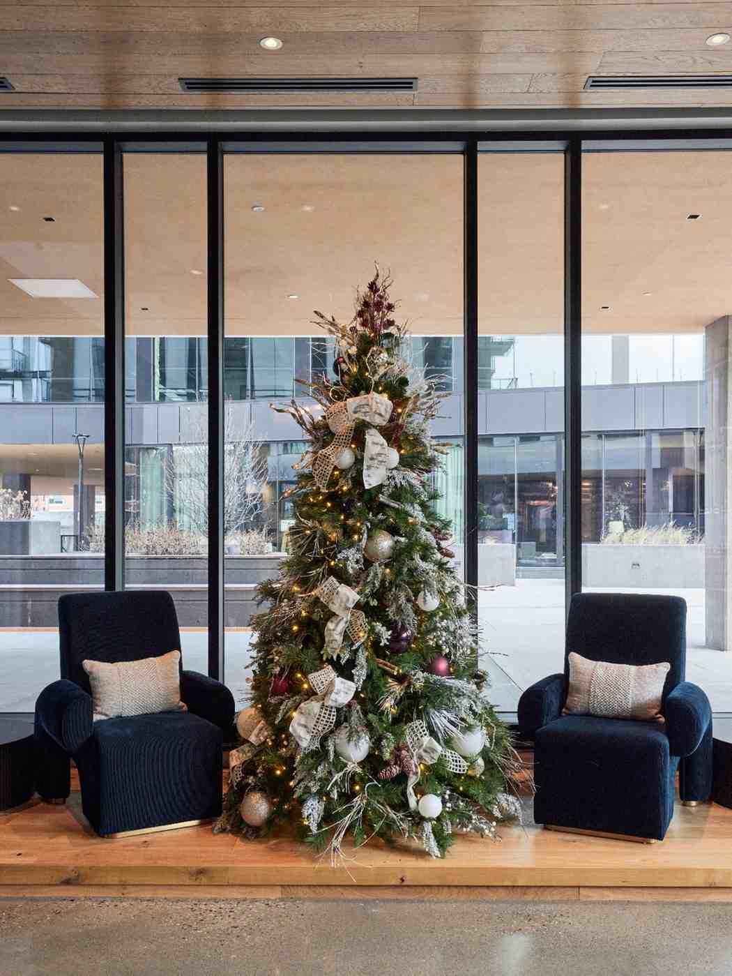 Decorated Christmas tree with two lounge chairs in a modern lobby.