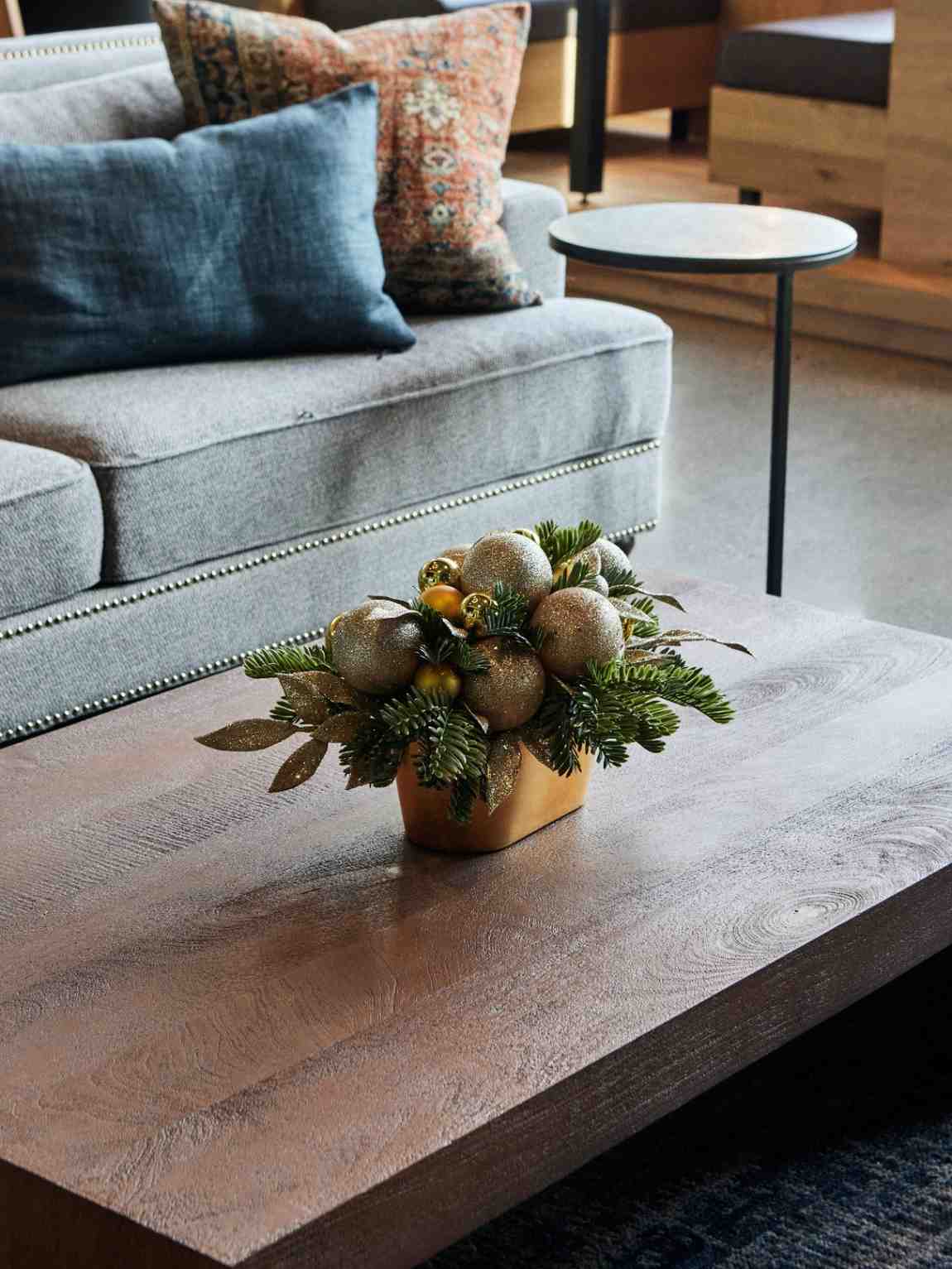 Holiday centerpiece with gold ornaments and greenery on a coffee table.