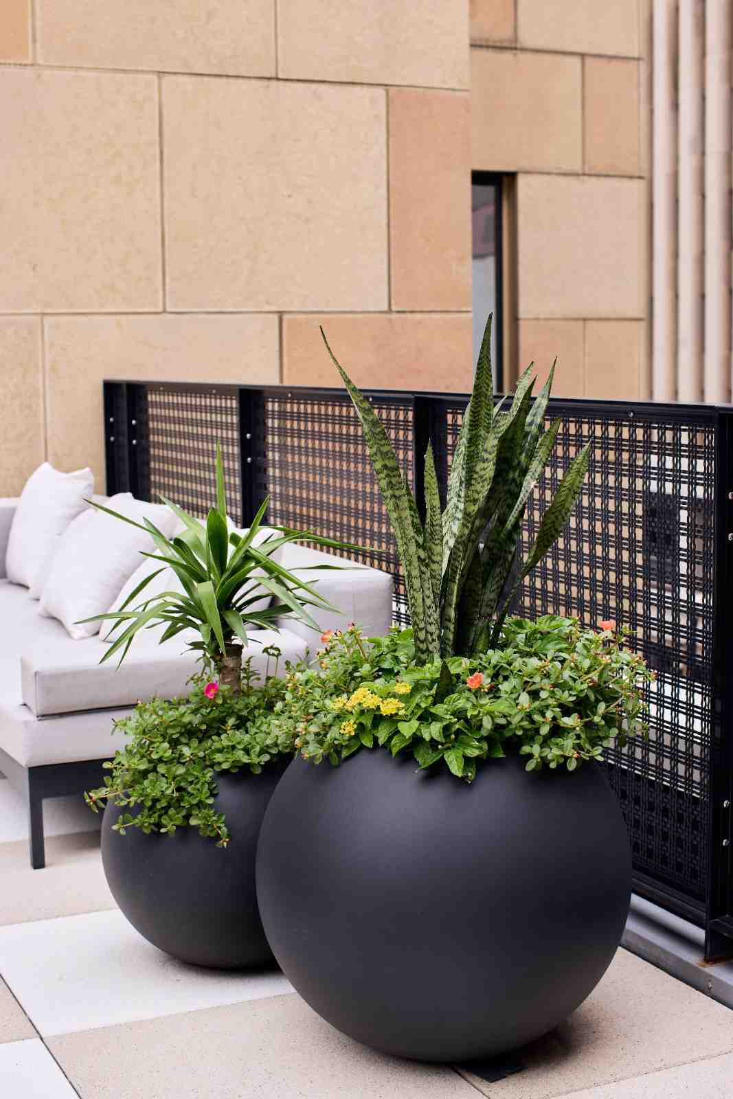 Modern outdoor planters with lush green plants beside a light gray patio sofa