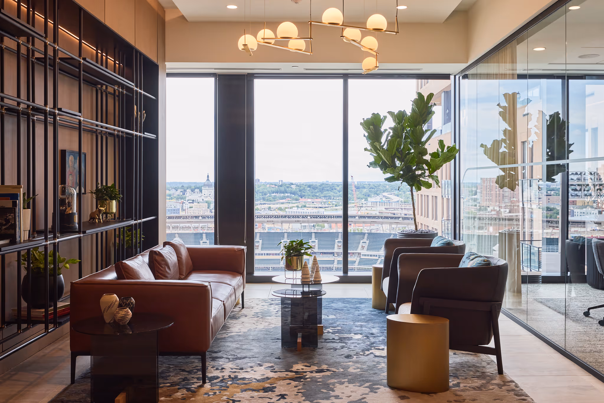 Modern office lounge with large fiddle leaf fig plant, leather sofa, and city skyline view.