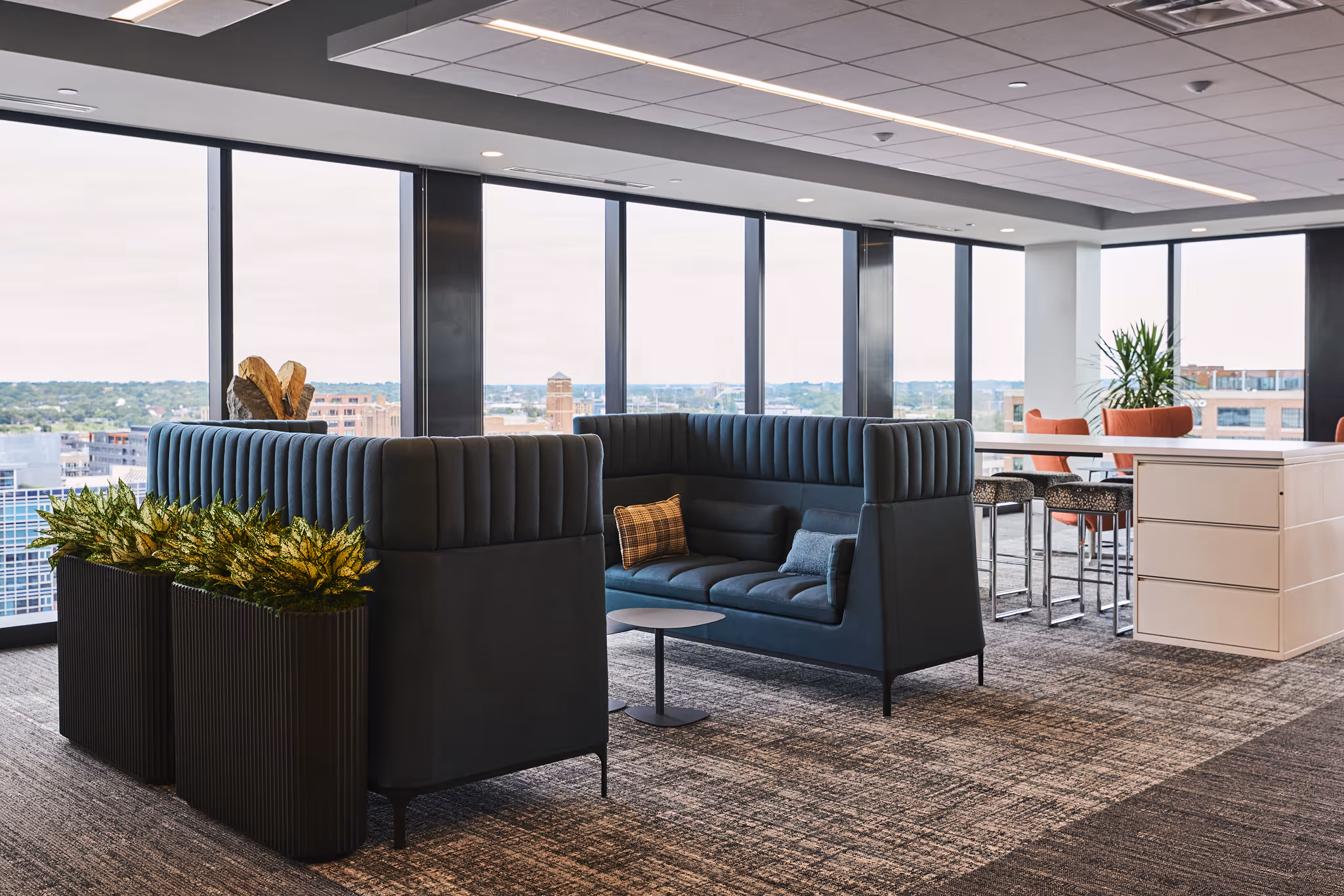 “Modern office lounge with large windows, high-back seating, and decorative indoor planters by Plants by Design
