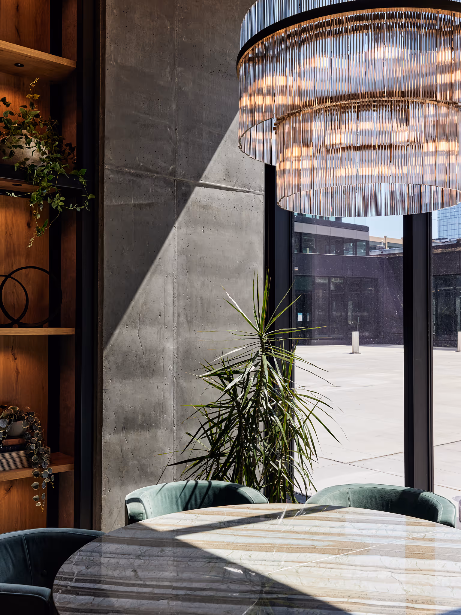 Indoor dining nook with a tall dracaena plant beside a large window, styled with a modern chandelier and marble table.