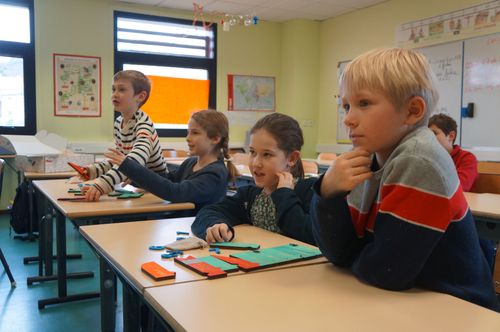 Des garçons et filles enthousiastes dans une salle de classe de primaire jouent à un jeu de programmation sans écran, Code en Bois.