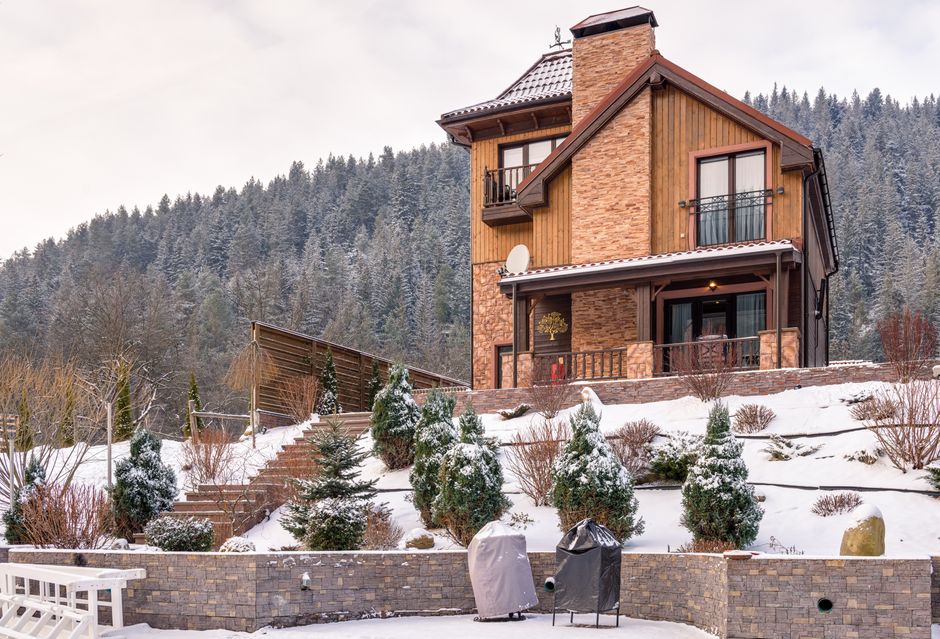 Charming wooden lodge surrounded by snow-covered forest under winter skies.