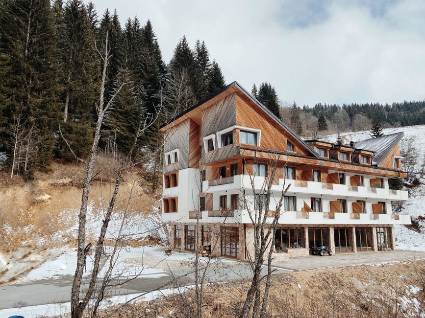 A large modern chalet nestled in a snowy mountain landscape surrounded by evergreen trees.