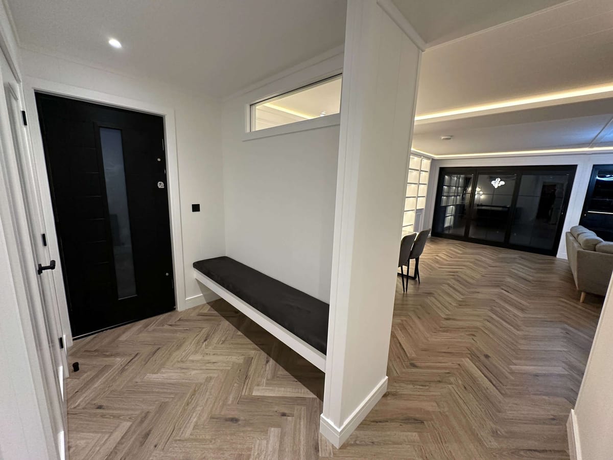 Modern Interior with Black Door, Herringbone Flooring, and Cozy Living Space Featuring Built-In Shelving, Dining Area, and Comfortable Gray Sofa