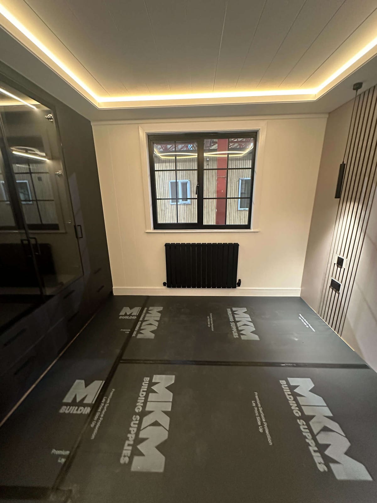 Modern Room Under Renovation with LED Ceiling Lights, Black Radiator, and Protective Floor Coverings from MKM Building Supplies