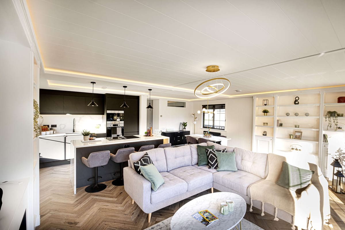 Modern Open-Plan Living Room and Kitchen with Sleek Black and White Fixtures, L-Shaped Sofa, and Elegant Lighting Fixtures, Featuring Built-In Shelving and Herringbone Wood Flooring