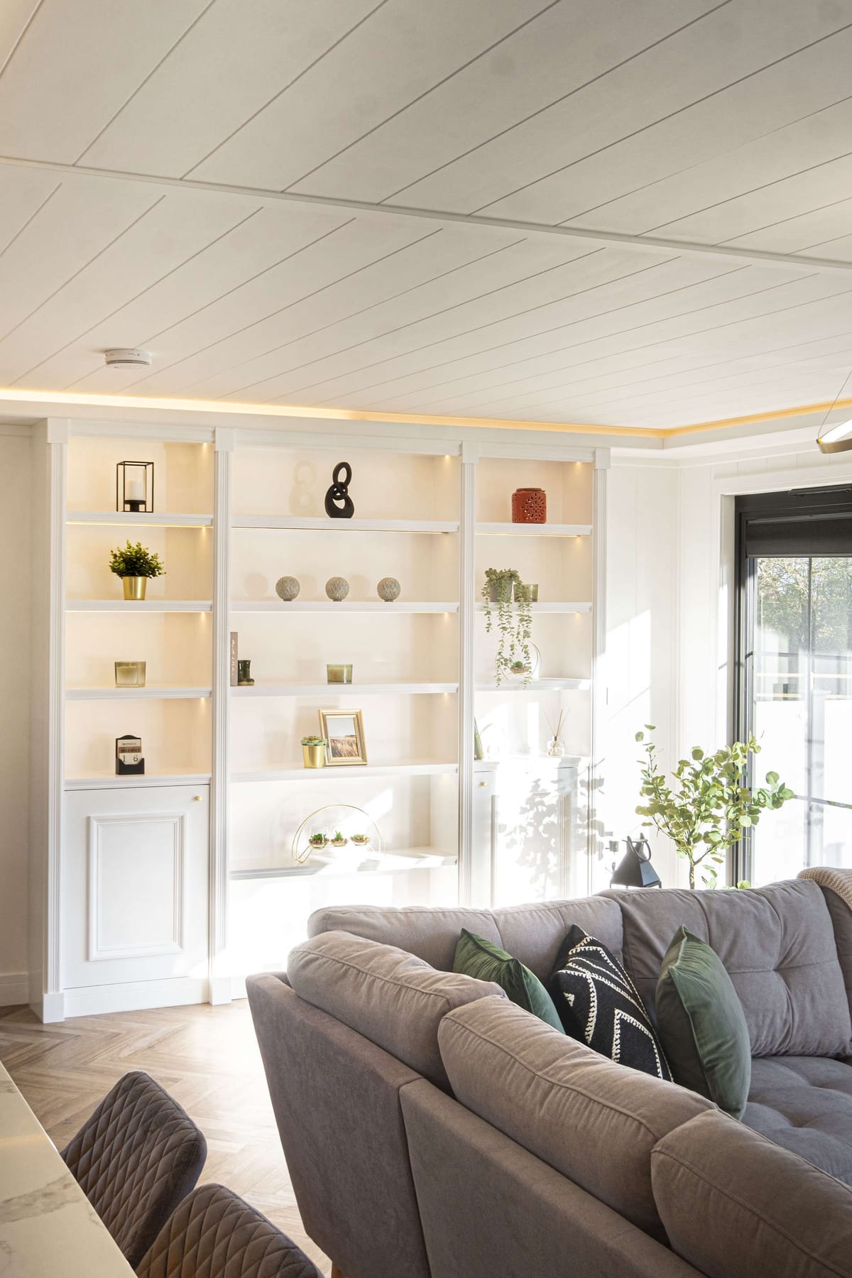 Modern Living Room with Built-In White Shelving, Plush Gray Sectional Sofa, Green Accent Pillows, and Abundant Natural Light from Large Window