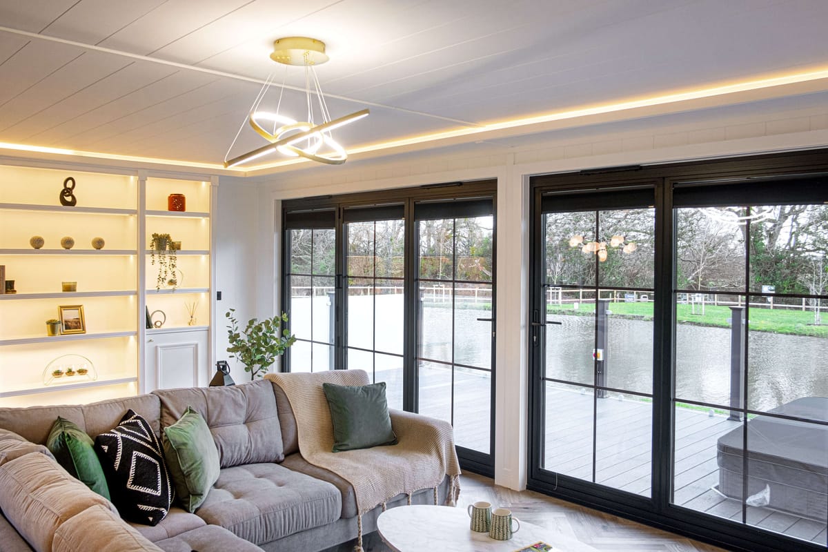 Modern Living Room with Cozy Gray Sectional Sofa, Elegant Pendant Light Fixture, and Large Glass Doors Offering Scenic Lake View, Featuring Built-In Shelving with Decorative Items and Plants