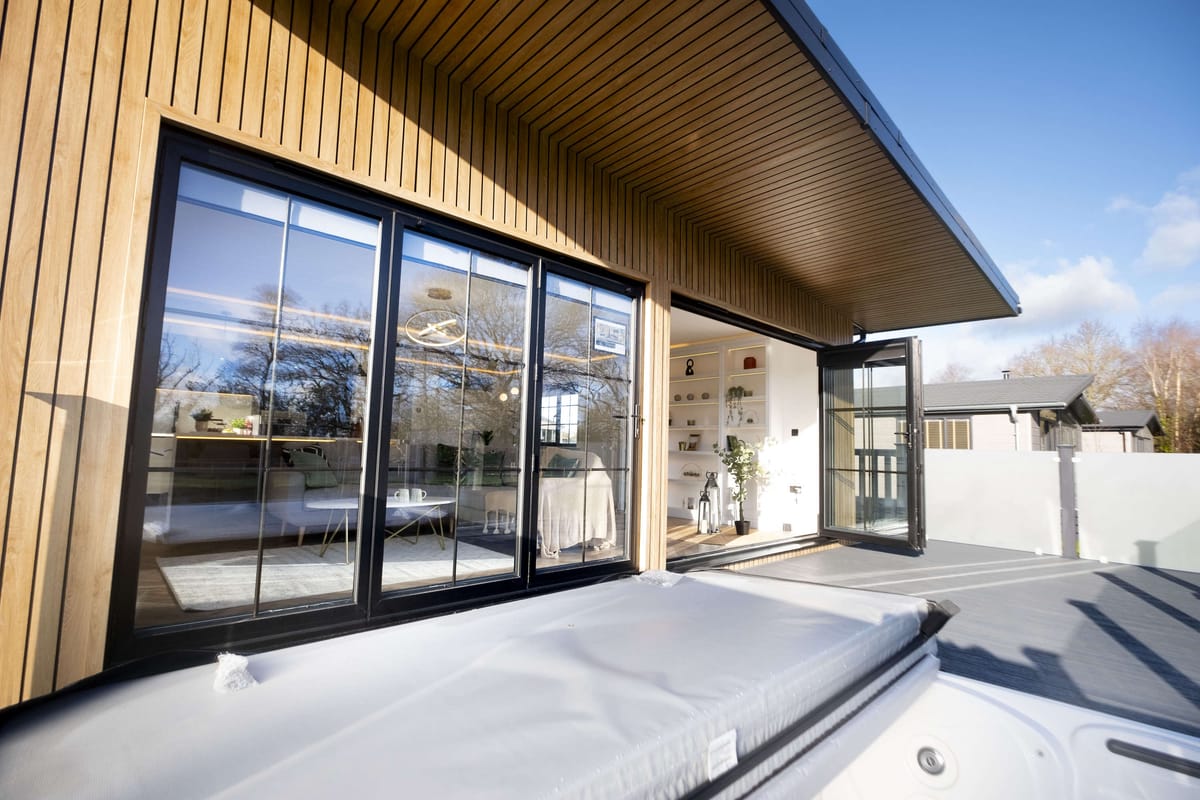 Modern Wooden House Exterior with Floor-to-Ceiling Glass Doors and Outdoor Hot Tub on Spacious Deck Under Clear Blue Sky