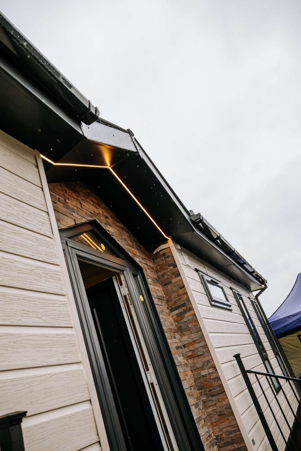 Modern Tiny House Exterior with Stone and Siding Facade Featuring Recessed Lighting and Black Trim Under Overcast Sky