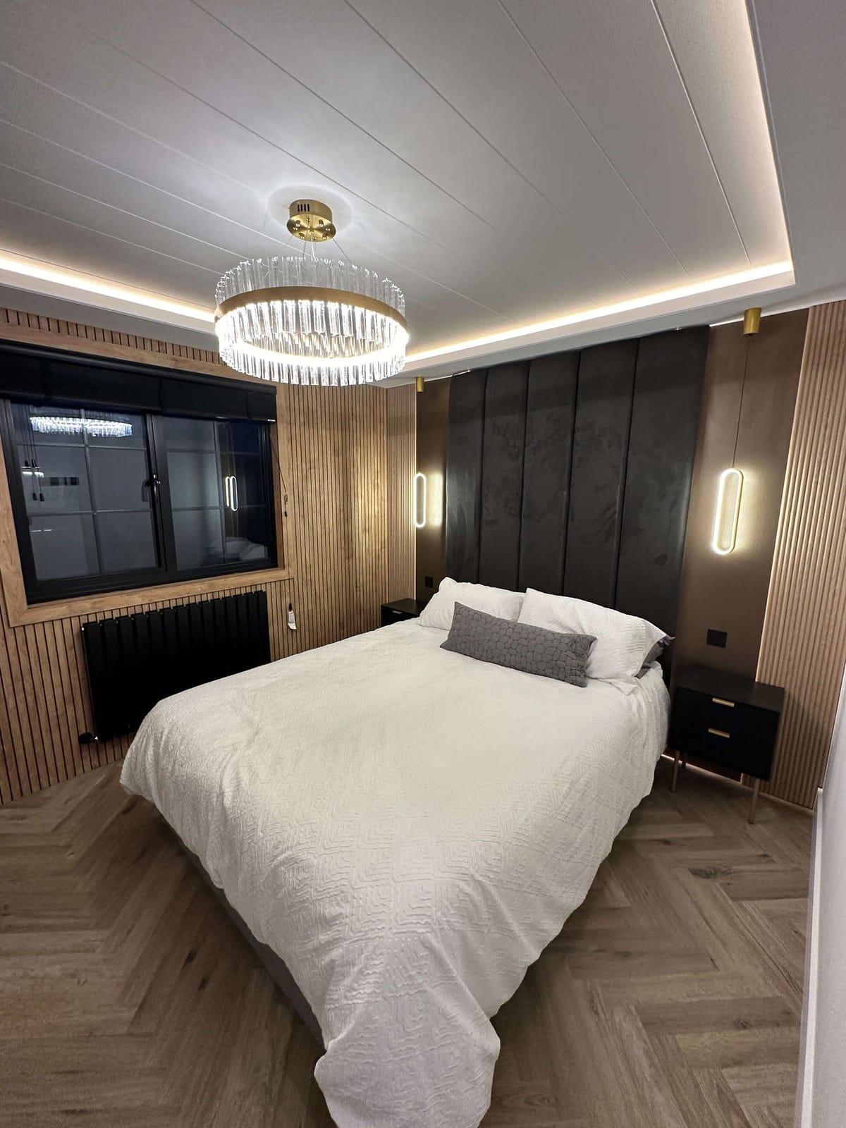Modern Bedroom with Elegant Crystal Chandelier, White Textured Bedding, Wood Paneling, and Soft Ambient Lighting