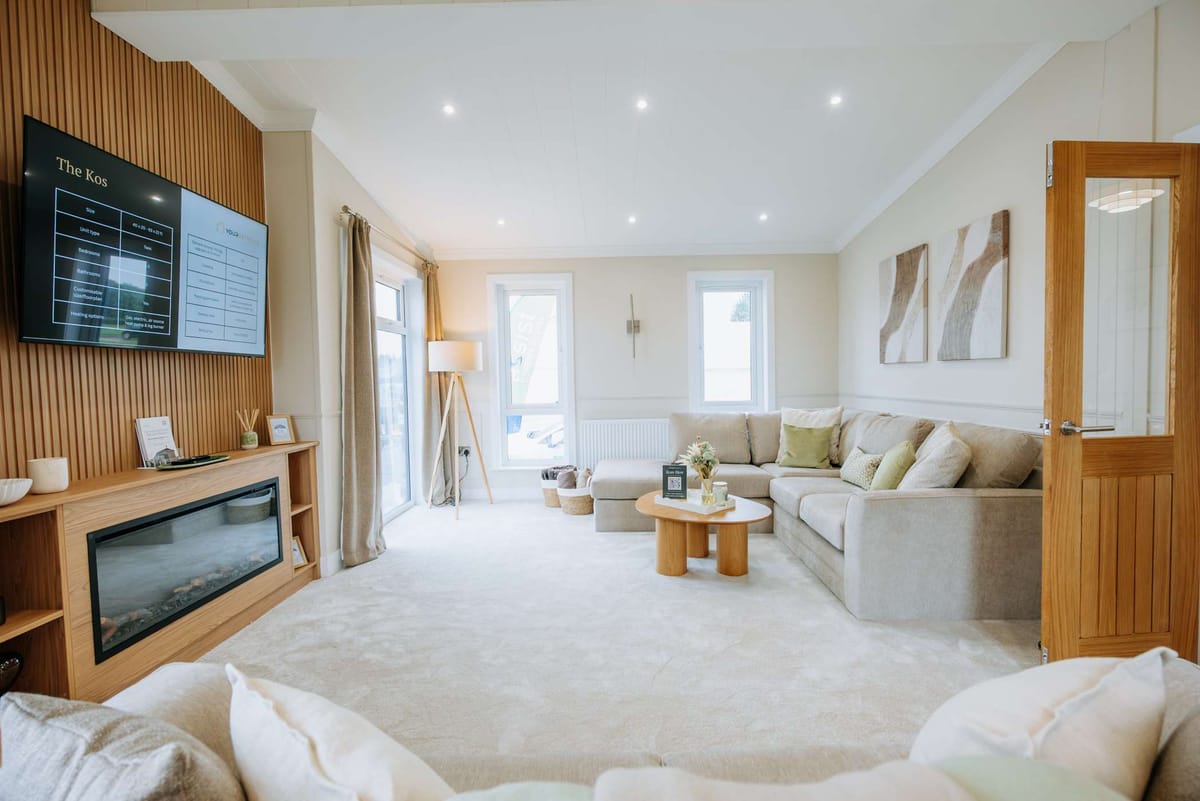 Bright and Modern Living Room with Neutral Tones Featuring a Sleek Wall-Mounted TV, Cozy Corner Sofa, Wooden Coffee Table, Large Windows with Sheer Curtains, Contemporary Art, and Elegant Lighting Accents