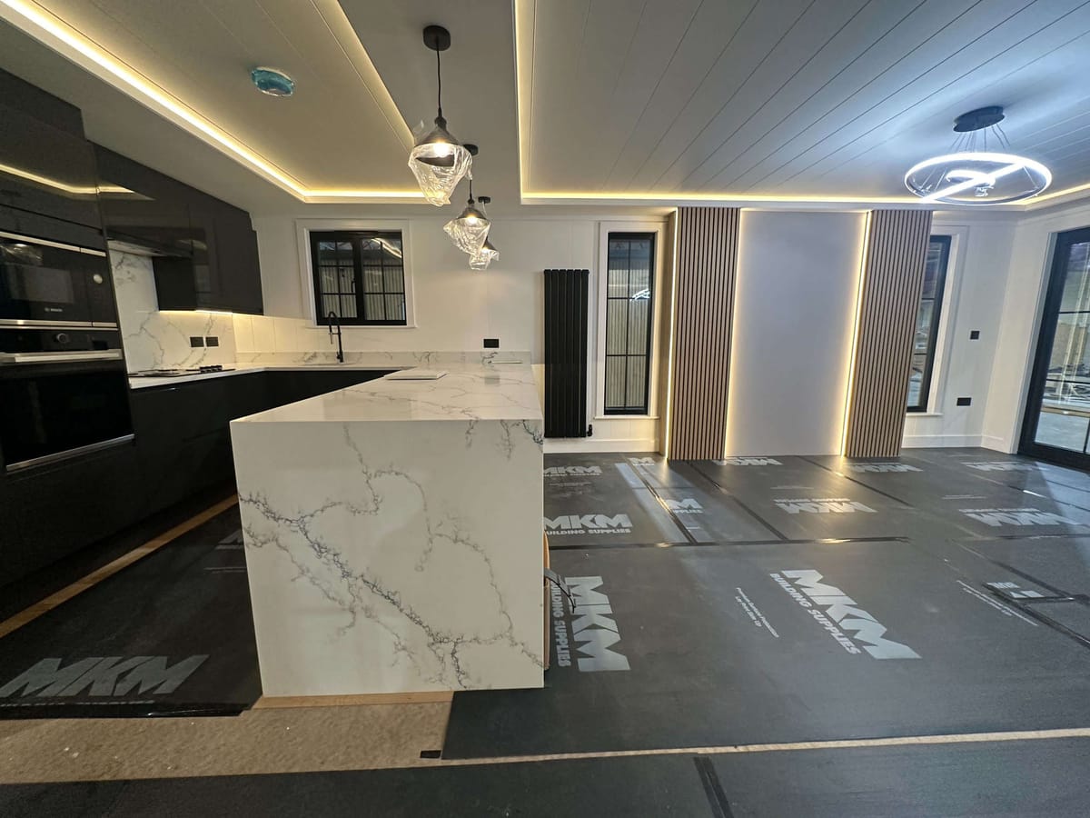 Modern Kitchen with Marble Island, Black Cabinets, and Ambient Lighting Featuring Pendant Lamps and Wooden Slat Accents